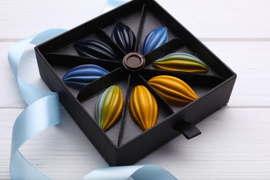 Photo of Box of tasty chocolate candies and ribbon on white wooden table, closeup