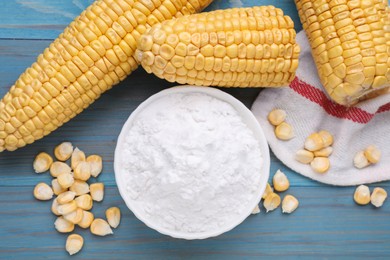 Bowl with corn starch, ripe cobs and kernels on light blue wooden table, flat lay