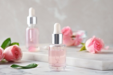 Bottles with rose essential oil and flowers on marble table