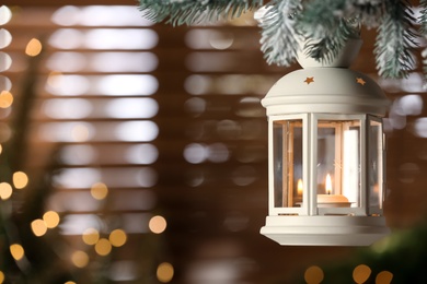 Photo of Beautiful Christmas lantern with burning candle hanging on fir tree branch in room. Space for text