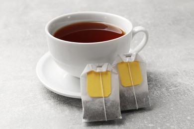 Tea bags and cup of aromatic drink on grey textured table, closeup