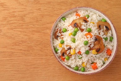 Photo of Bowl of delicious rice with vegetables on wooden table, top view. Space for text