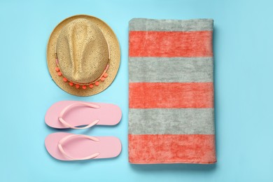 Photo of Beach towel, flip flops and hat on light blue background, flat lay