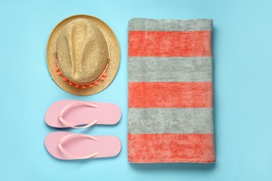 Beach towel, flip flops and hat on light blue background, flat lay