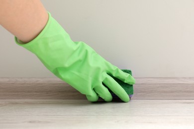 Woman in protective glove cleaning plinth with sponge indoors, closeup