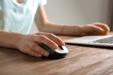 Woman using computer mouse with laptop at table, closeup