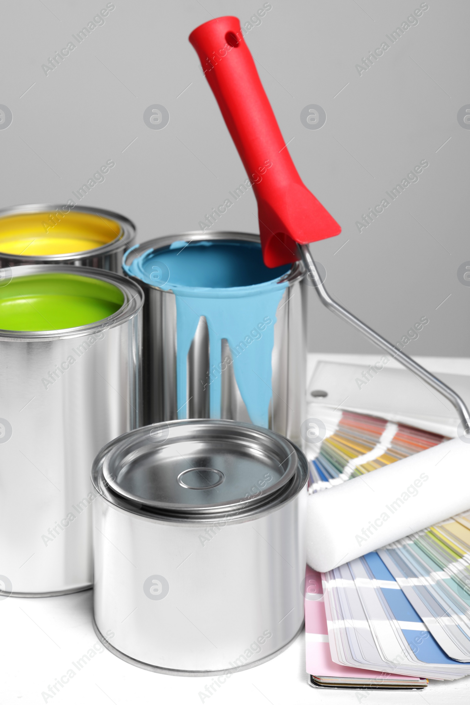 Photo of Cans of paints, roller and palette on white wooden table