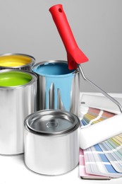 Cans of paints, roller and palette on white wooden table