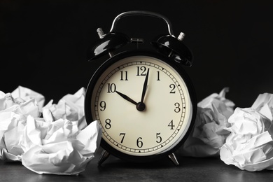 Photo of Crumpled paper balls and alarm clock on table against dark background