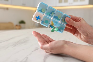 Woman with pills and organizer at white marble table, closeup