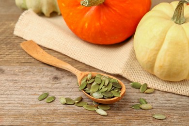 Spoon with peeled seeds and fresh pumpkins on wooden table