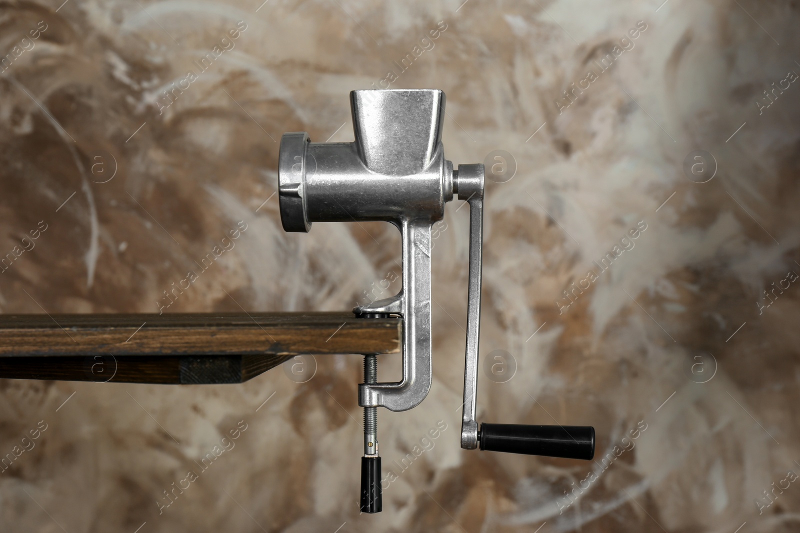 Photo of Metal manual meat grinder on wooden table against color background