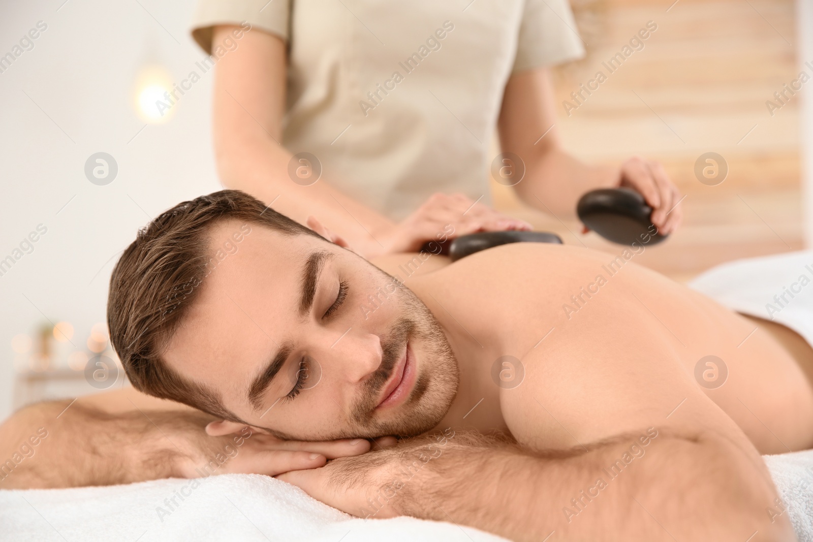 Photo of Handsome man receiving hot stone massage in spa salon