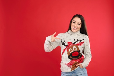 Photo of Young woman in Christmas sweater on red background, space for text