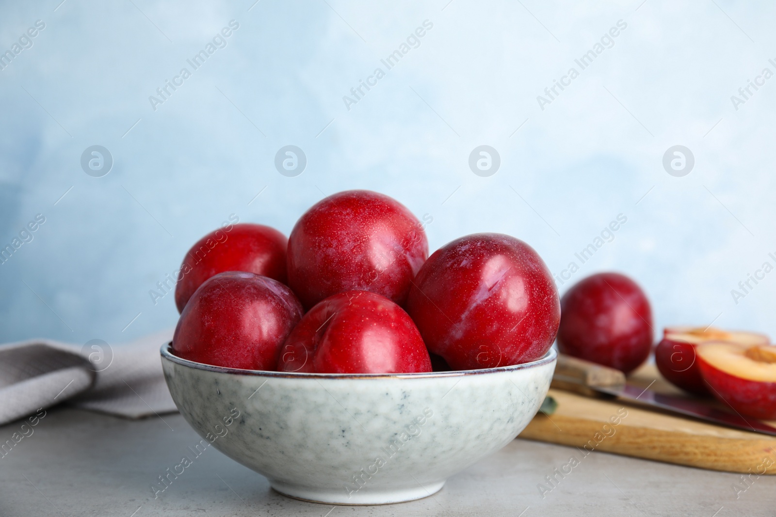 Photo of Delicious ripe plums in bowl on grey table