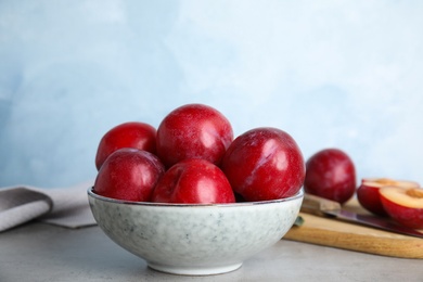 Delicious ripe plums in bowl on grey table