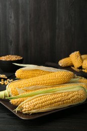 Tasty fresh corn cobs on black wooden table