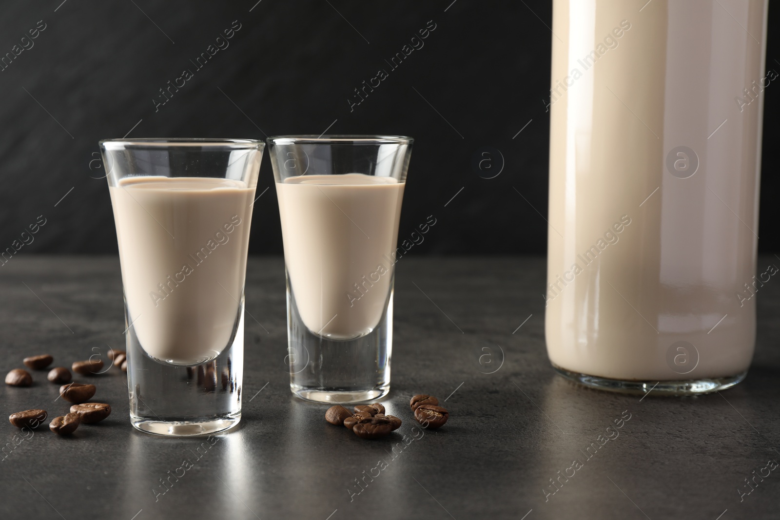 Photo of Coffee cream liqueur in glasses, bottle and beans on grey table