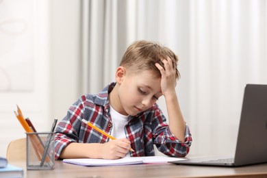 Photo of Little boy suffering from headache while studying at wooden desk indoors