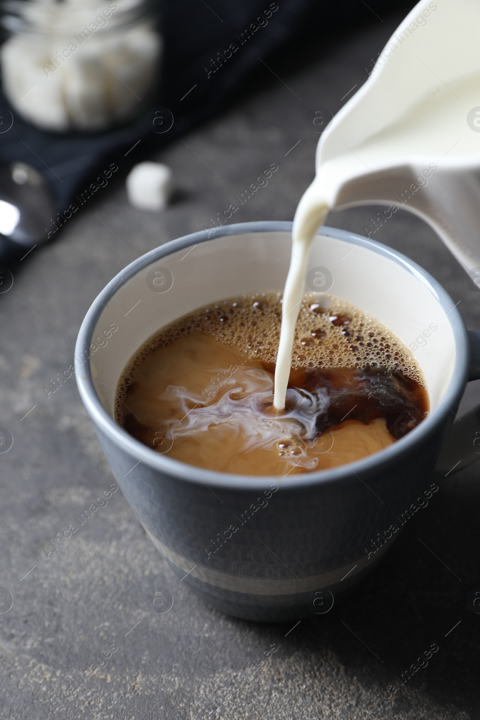 Photo of Pouring milk into cup of coffee on grey table, closeup