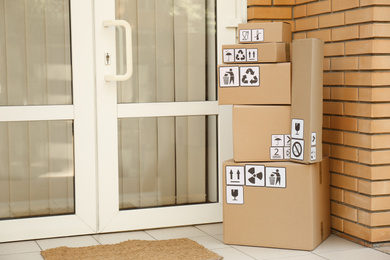 Photo of Cardboard boxes with different packaging symbols on porch near entrance, space for text. Parcel delivery