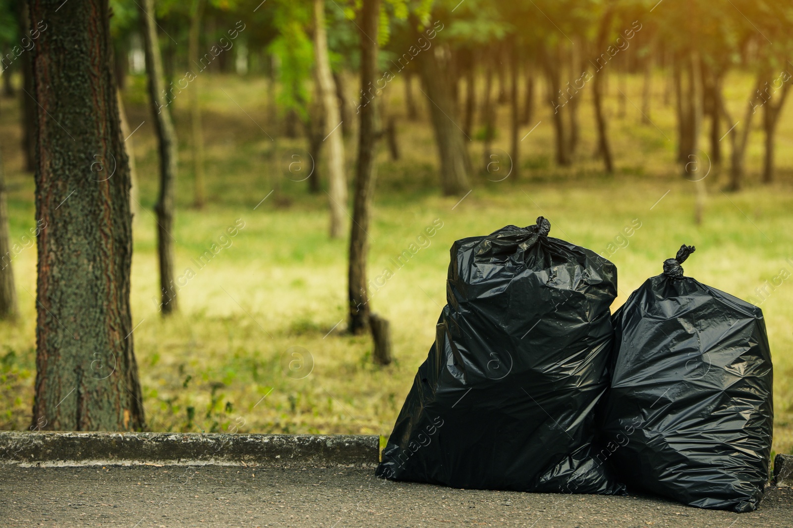 Photo of Trash bags full of garbage on pavement in park. Space for text