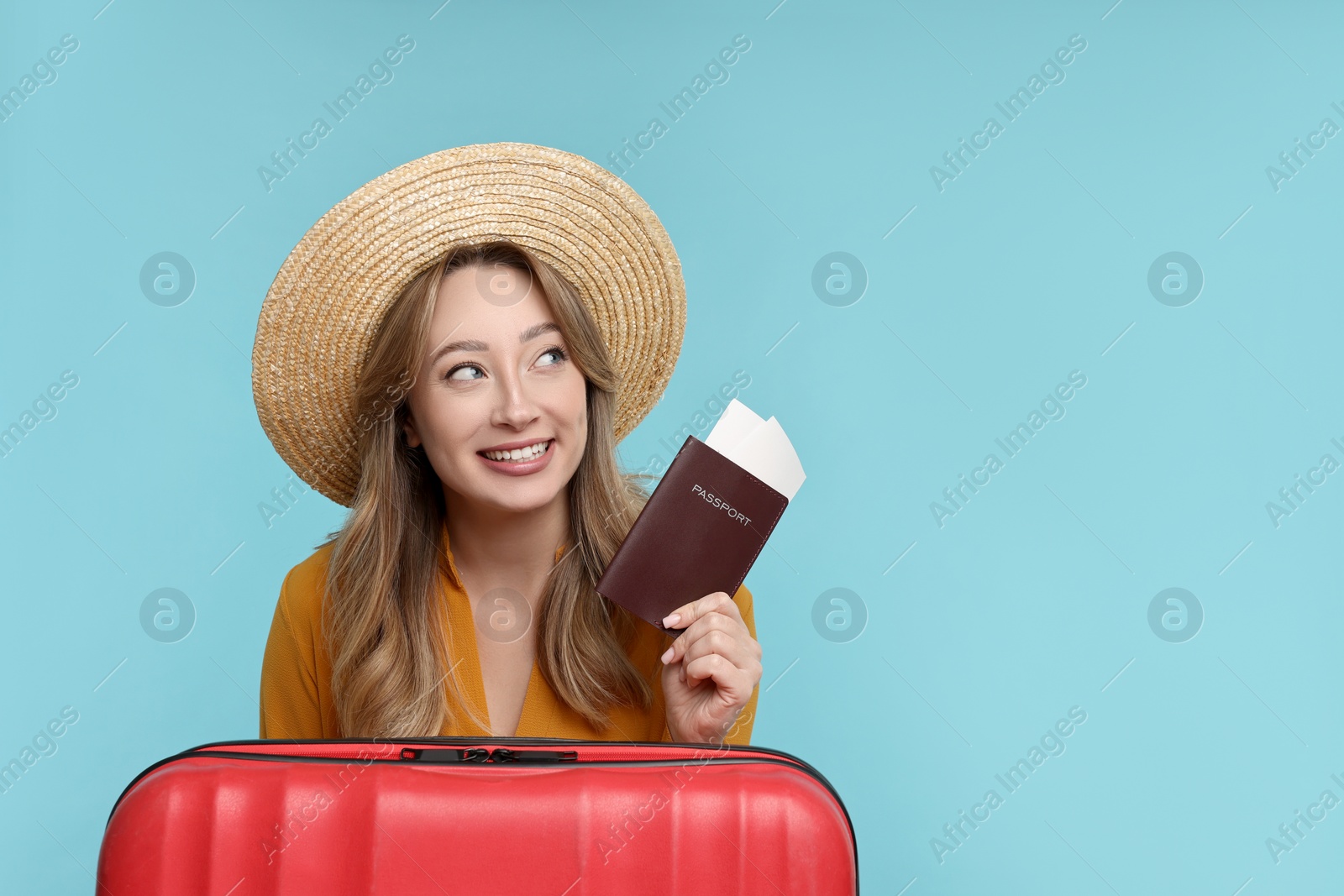 Photo of Happy young woman with passport, ticket and suitcase on light blue background, space for text
