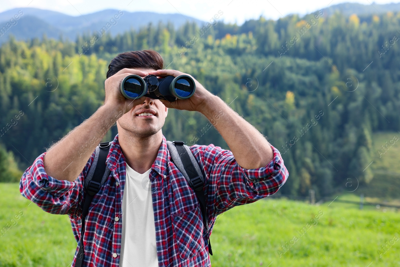 Photo of Man with backpack looking through binoculars in mountains