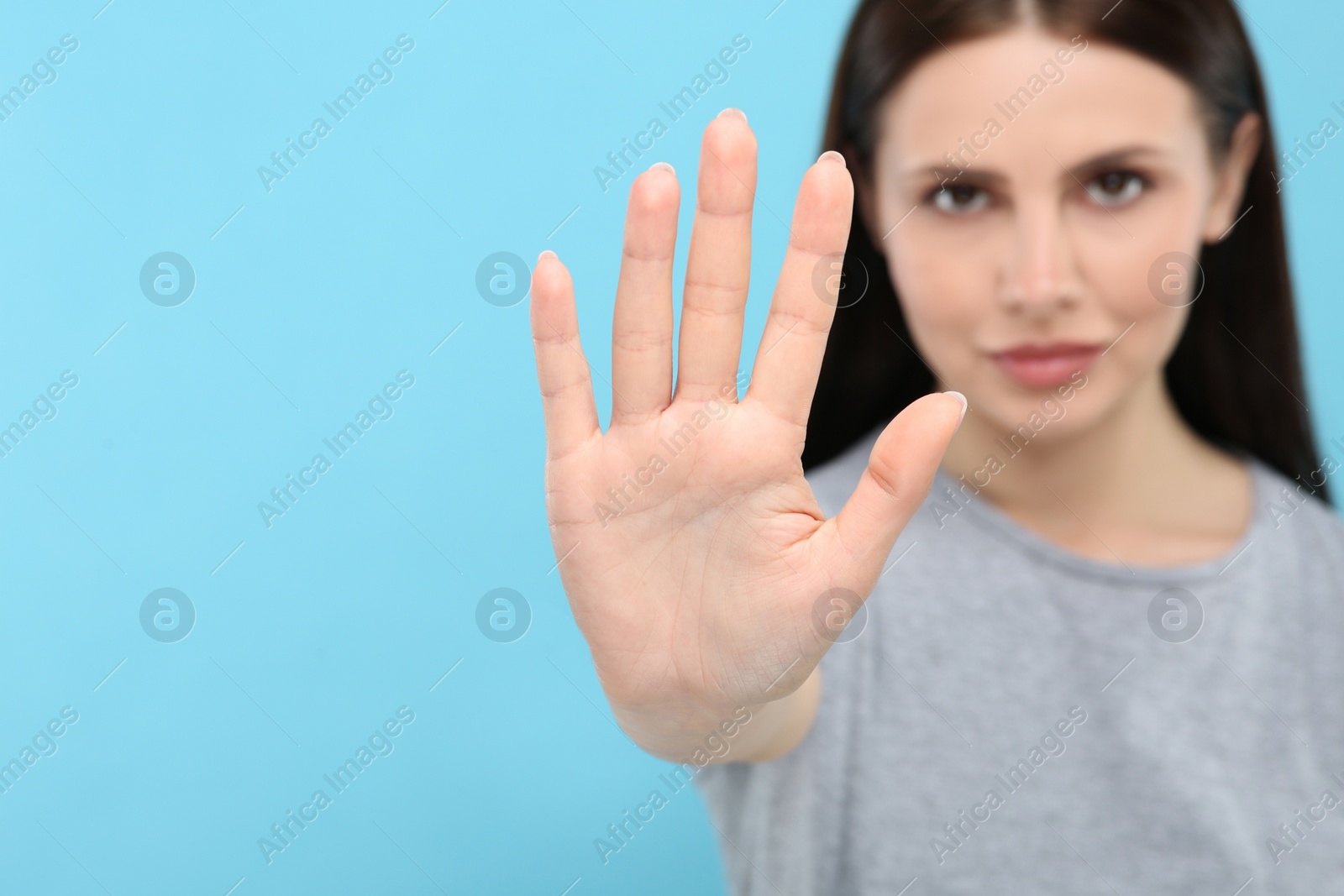 Photo of Woman showing stop gesture on light blue background, selective focus. Space for text