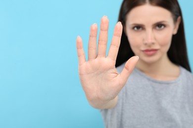 Woman showing stop gesture on light blue background, selective focus. Space for text