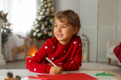 Cute child writing letter to Santa Claus at table indoors. Christmas tradition