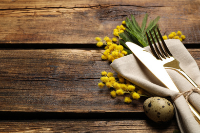 Closeup view of cutlery set with quail egg and floral decor on wooden table, space for text. Easter celebration