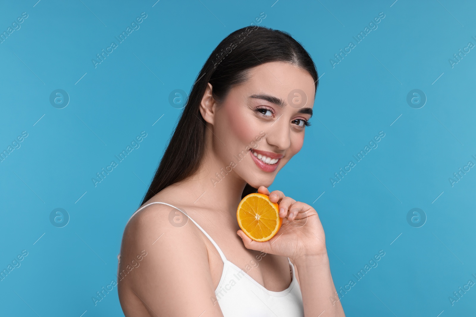 Photo of Beautiful young woman with piece of orange on light blue background