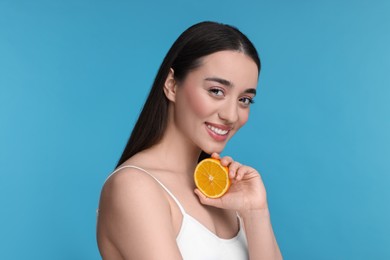 Beautiful young woman with piece of orange on light blue background