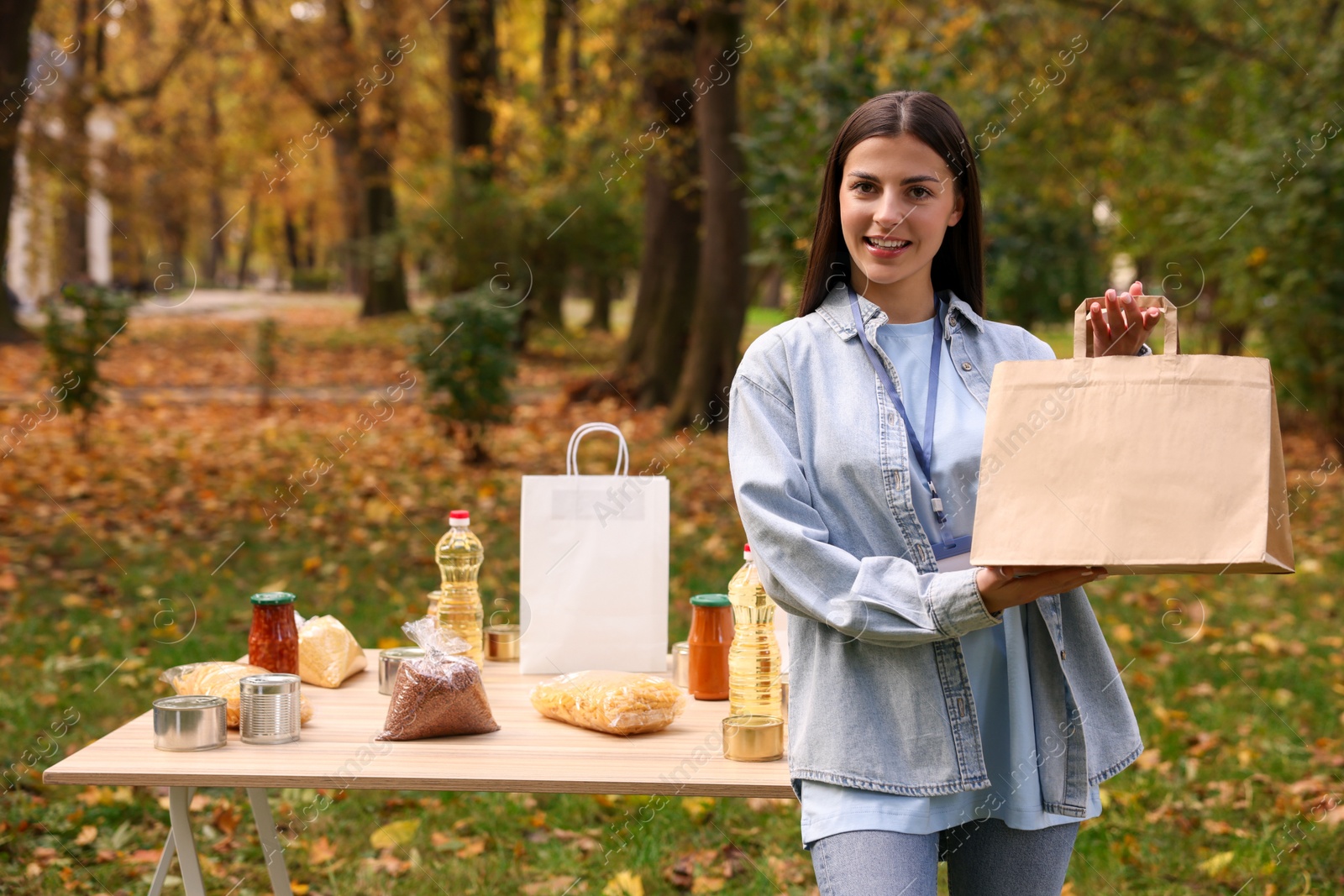 Photo of Portrait of volunteer with paper bag and food products on table in park