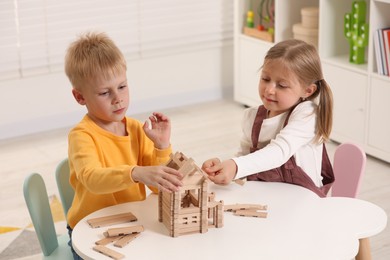 Little boy and girl playing with wooden house at white table indoors. Children's toys