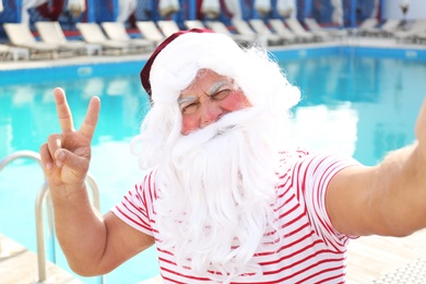 Photo of Authentic Santa Claus taking selfie near swimming pool outdoors