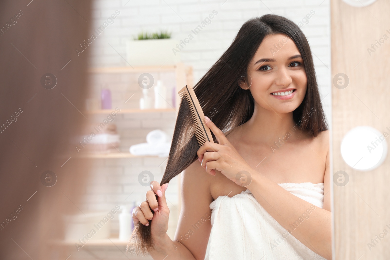 Photo of Beautiful young woman with hair brush looking into mirror in bathroom