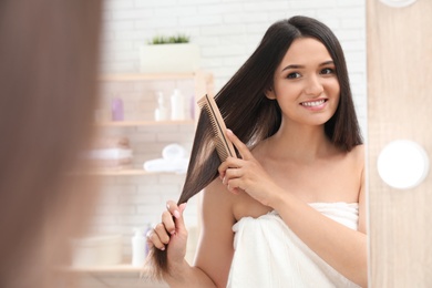 Photo of Beautiful young woman with hair brush looking into mirror in bathroom