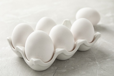 Photo of Raw chicken eggs in ceramic holder on light background