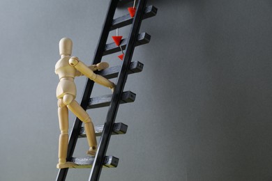 Photo of Overcoming barries for development and success. Wooden human figure climbing up toy ladder with pins near grey wall, space for text