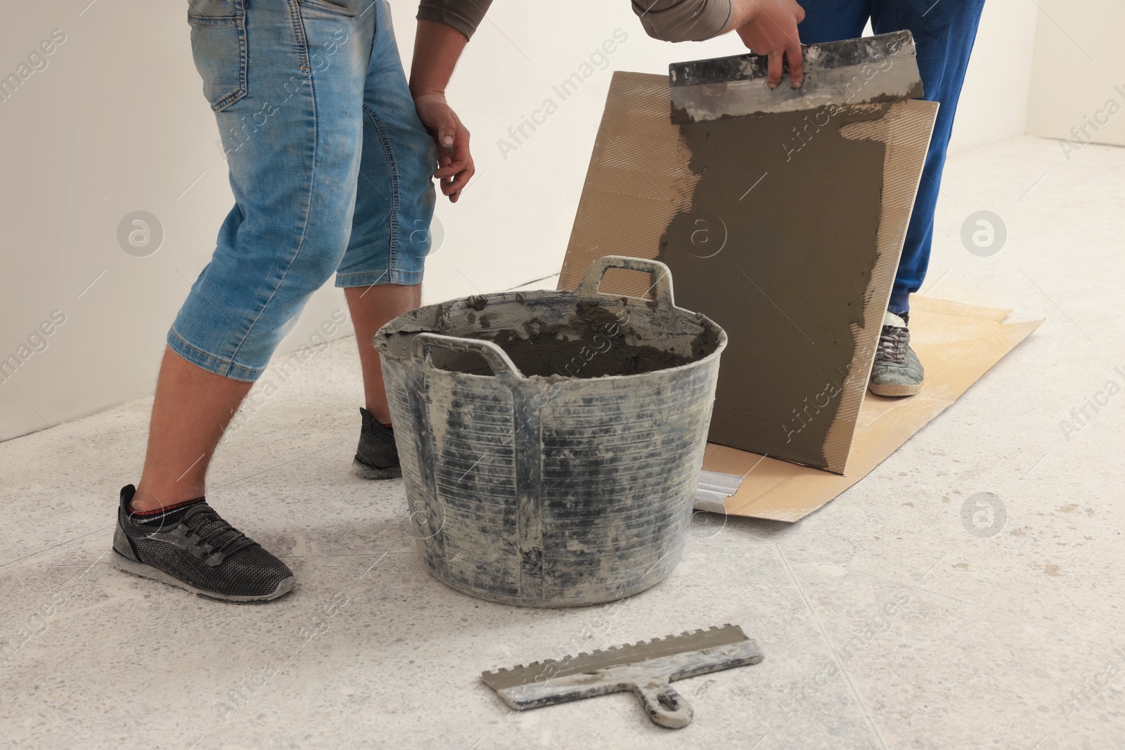 Photo of Worker spreading adhesive mix over tile with spatula, closeup