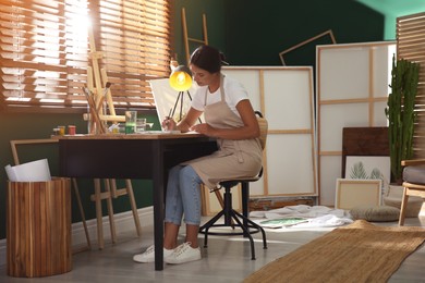 Photo of Young woman drawing with watercolors at table indoors