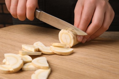 Woman cutting delicious fresh ripe parsnip at wooden board, closeup