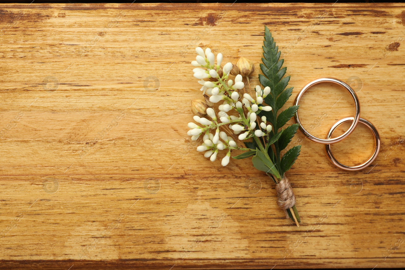Photo of Small stylish boutonniere and rings on wooden table, flat lay. Space for text