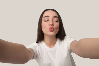 Photo of Young woman taking selfie and blowing kiss on white background