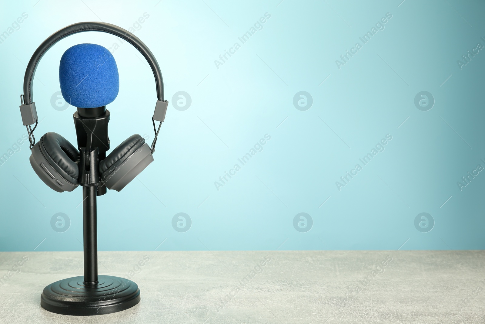 Photo of Microphone and modern headphones on grey table against light blue background, space for text