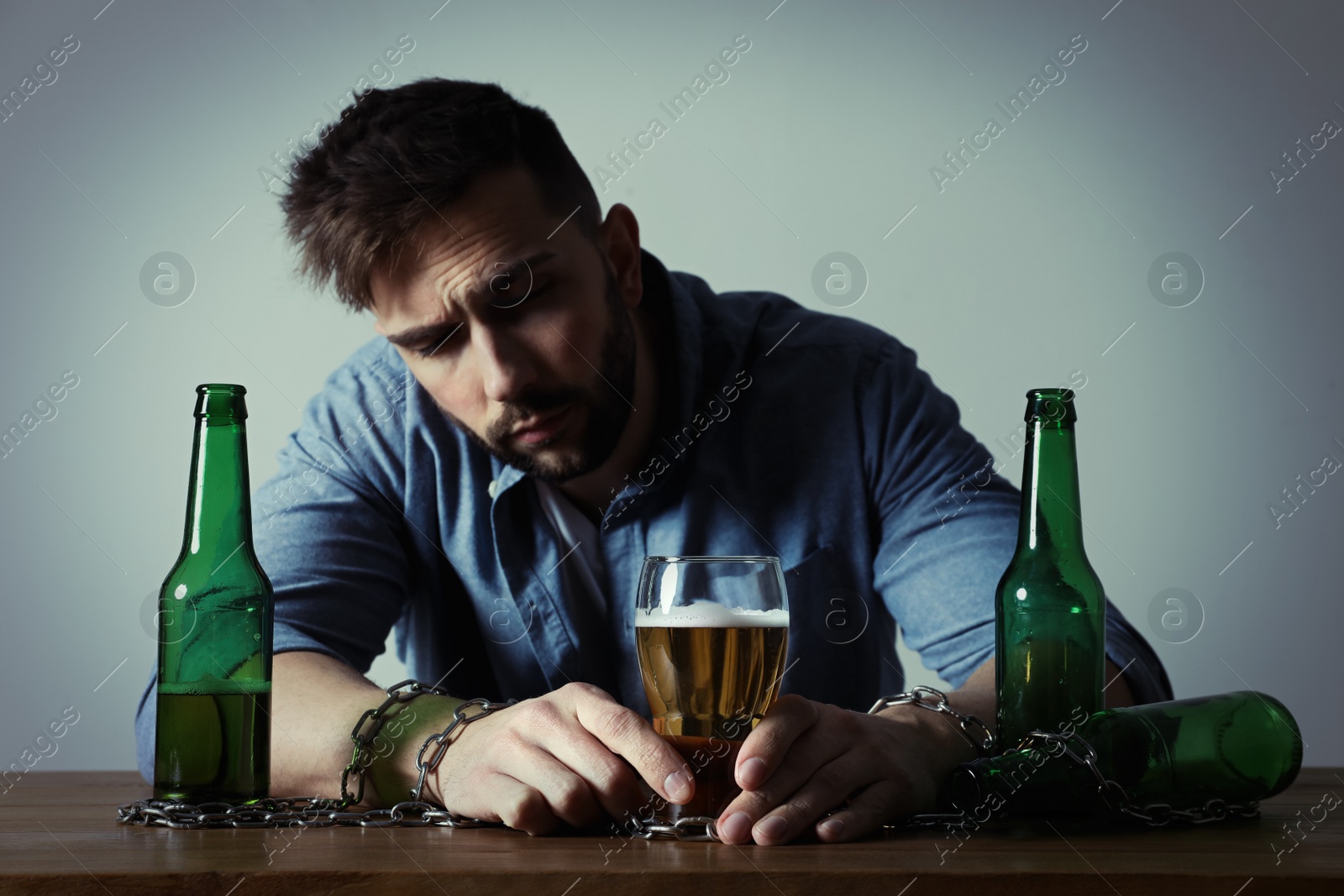 Photo of Addicted man chained to glass of alcoholic drink at wooden table