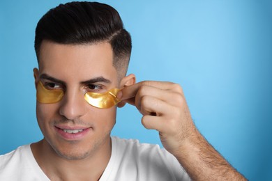 Photo of Man applying golden under eye patch on light blue background