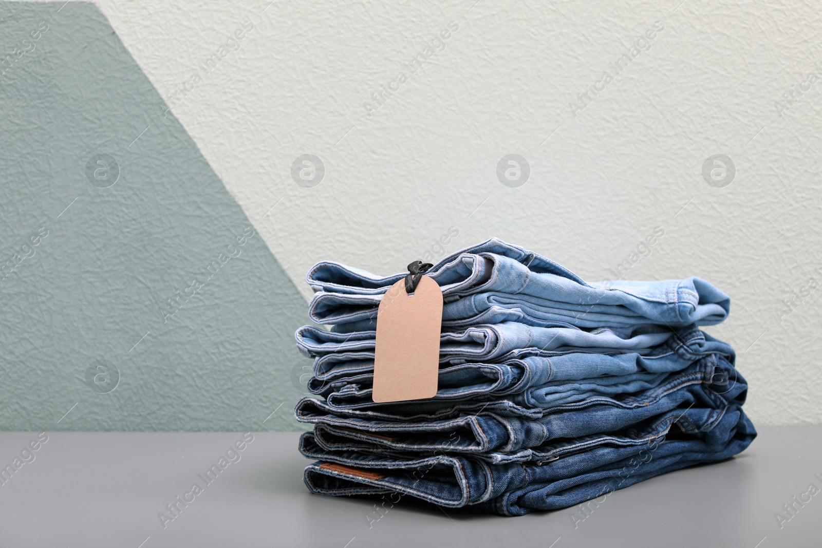 Photo of Stack of stylish jeans with tag on table against color wall